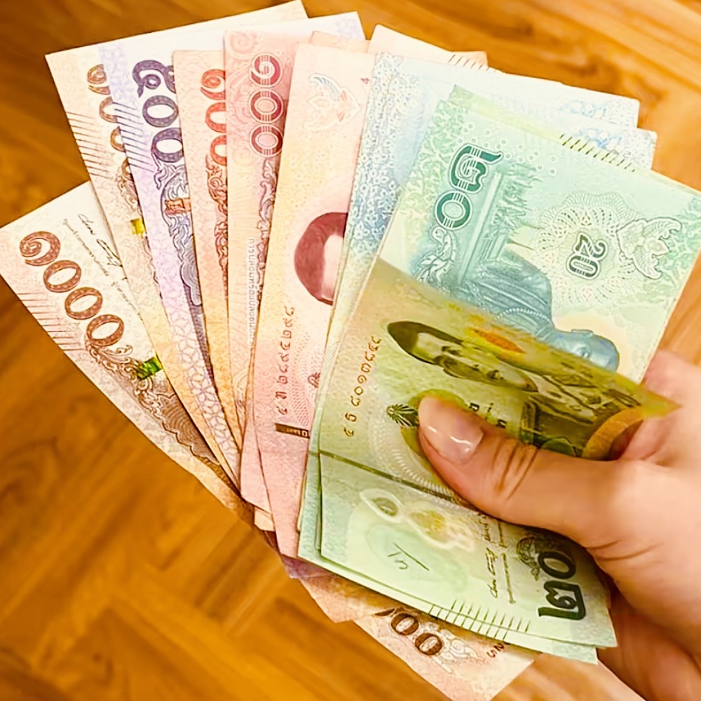 A hand fanning out Thai baht banknotes