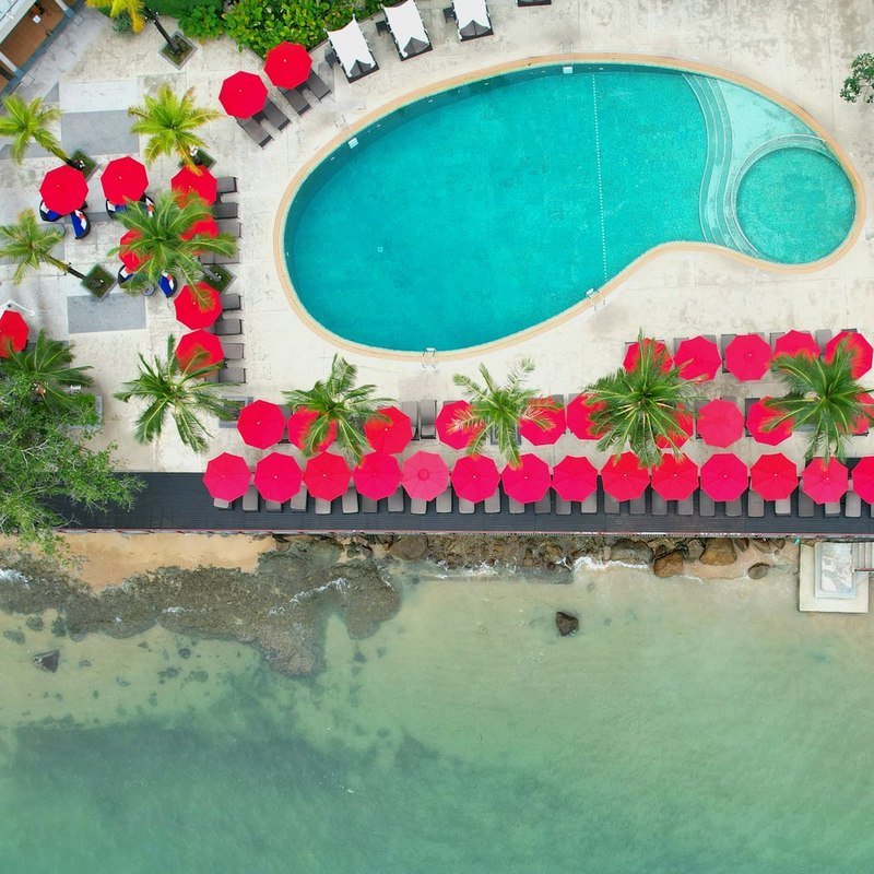Aerial view of a resort pool and red sun loungers beside the sea